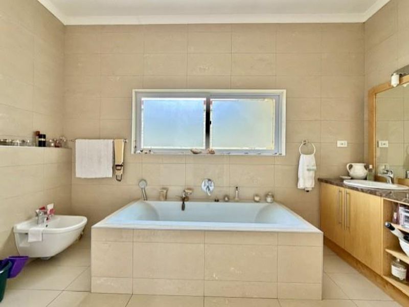 A spacious bathroom featuring a built-in bathtub, bidet, and vanity cabinet with neutral wall and floor tiling.