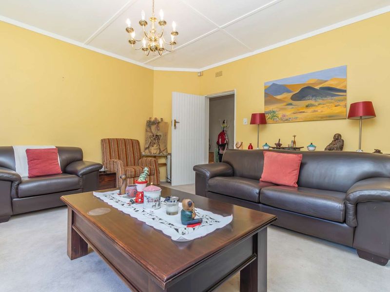 A comfortable living room featuring a classic chandelier, decorative ceiling cornice, and neutral carpeting, providing a functional space for relaxation.