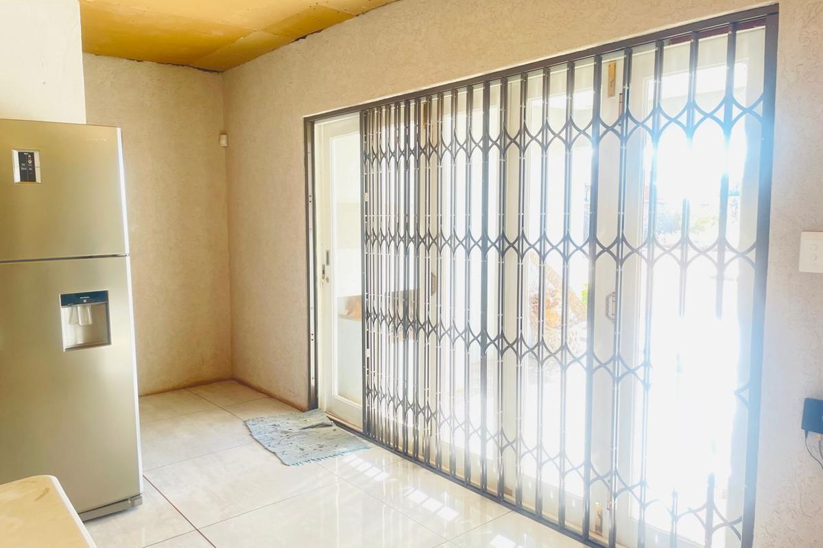 A kitchen area featuring tiled flooring and a sliding glass door secured with a metal security gate, leading to an outdoor space.