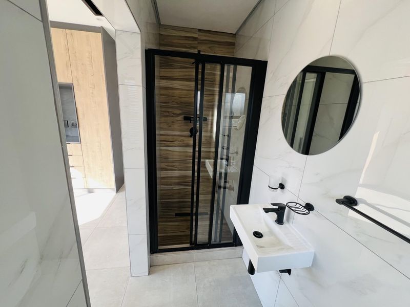 Modern bathroom featuring a sleek walk-in shower with black frame, wall-mounted basin, and contemporary marble-look wall tiling.