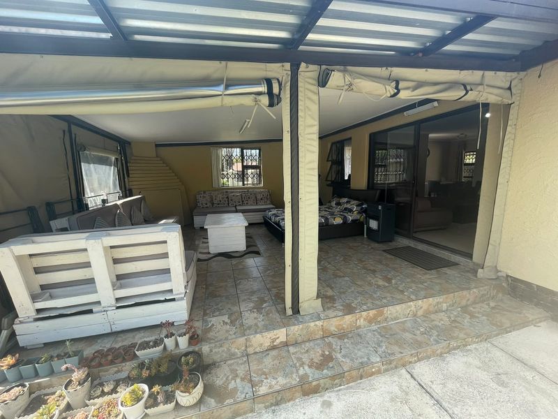 A covered outdoor patio area featuring tiled flooring, roll-up canvas blinds, and direct access to the interior living space through sliding glass doors.