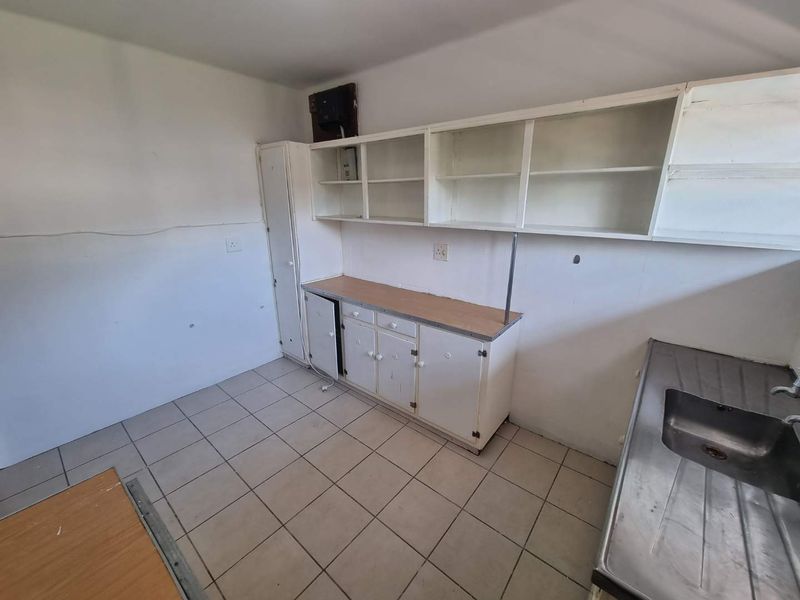 A functional scullery or utility area featuring built-in cabinetry, open shelving, and a stainless steel sink, requiring cosmetic updates to improve its condition.