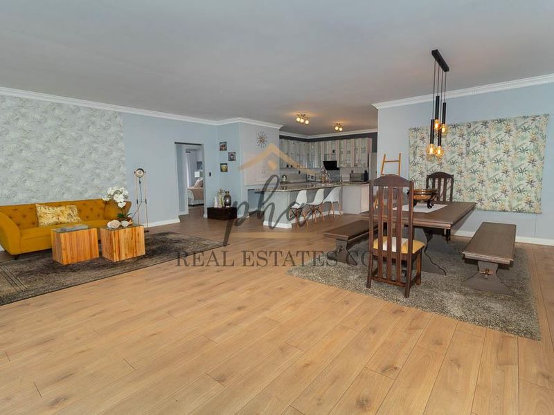 Spacious open-plan living and dining area featuring light wood-look laminate flooring, a modern kitchen island, and contemporary pendant lighting.