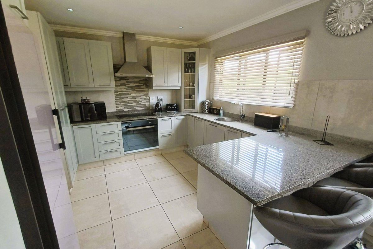 A well-maintained kitchen featuring granite countertops, built-in oven, electric hob, stainless steel extractor fan, and ample cabinetry with a breakfast nook.