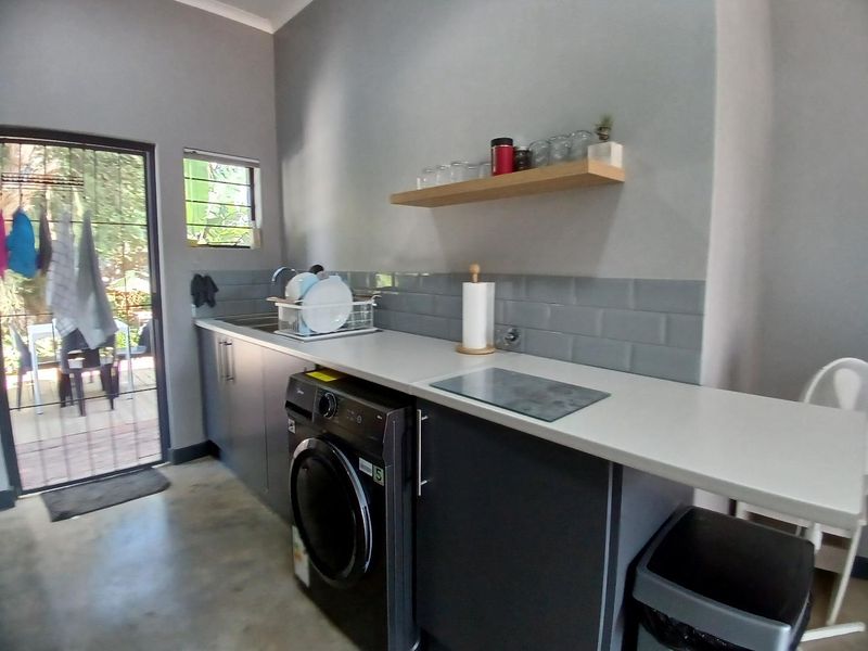 A functional laundry area featuring modern dark cabinetry, subway tile backsplash, polished concrete floors, and direct access to the outdoor patio.