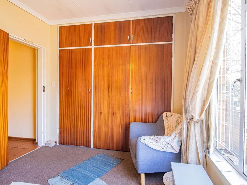 A bedroom featuring built-in wooden cupboards and a window with security bars, offering a functional space with potential for modernization.