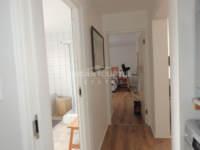 A view through a hallway connecting to a bathroom and bedroom, featuring laminate flooring and neutral wall finishes.