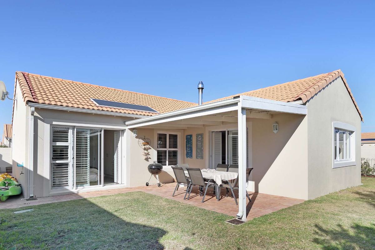 Rear view of the house featuring a covered patio with brick paving, sliding glass doors, and a well-maintained garden area.