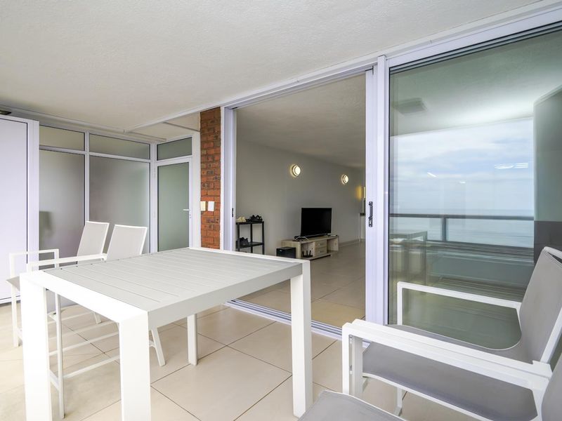 A spacious covered balcony featuring tiled flooring, an exposed brick accent, and large sliding glass doors that provide seamless access to the interior living area.