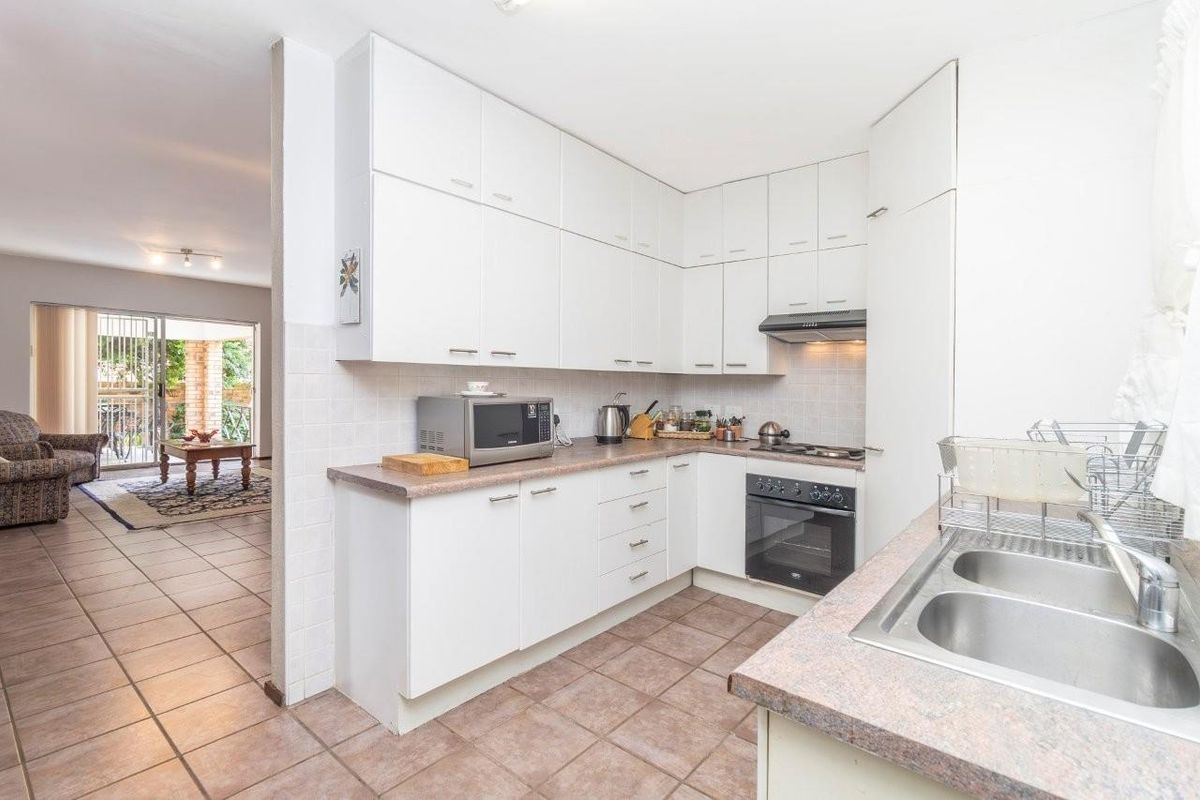 A functional kitchen featuring white cabinetry, laminate countertops, a built-in oven, and a hob, with an adjacent view into the living area.