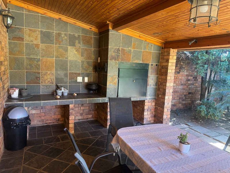 Covered patio area featuring a built-in braai, slate tile finishes, and exposed timber ceiling, providing a functional space for outdoor entertaining.