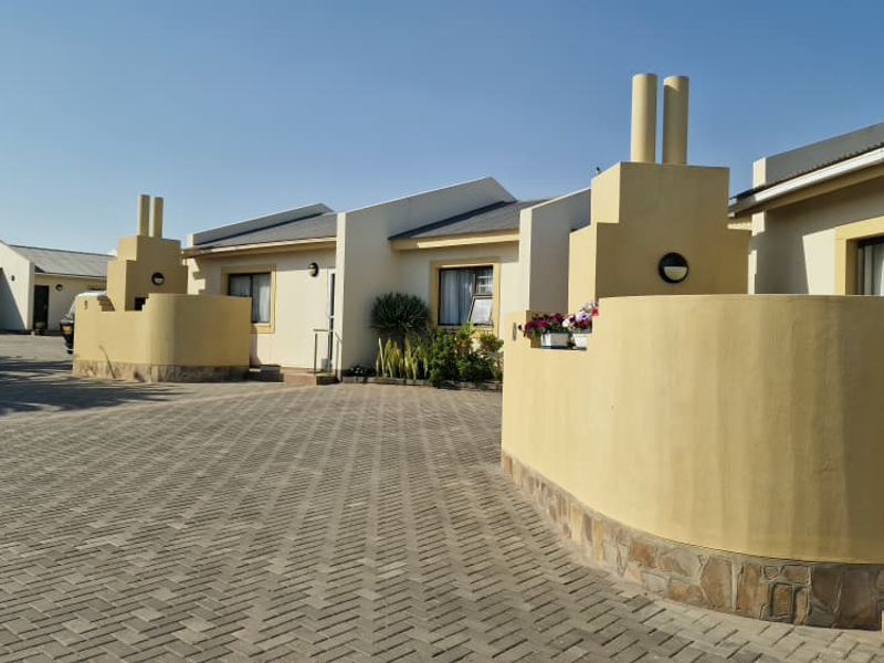 Front view of a townhouse complex featuring paved driveway access, cream-colored exterior walls with stone base detailing, and prominent chimney structures.