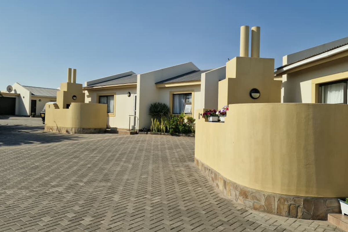 Front view of a townhouse complex featuring paved driveway access, cream-colored exterior walls with stone base detailing, and prominent chimney structures.