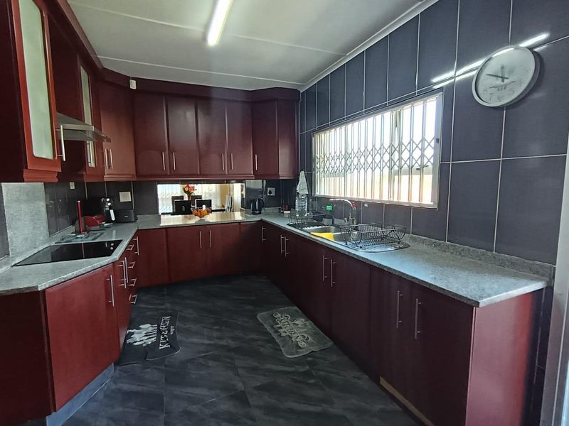A functional kitchen featuring dark wood cabinetry, granite-look laminate countertops, a stainless steel sink, and a built-in electric hob with an extractor fan.