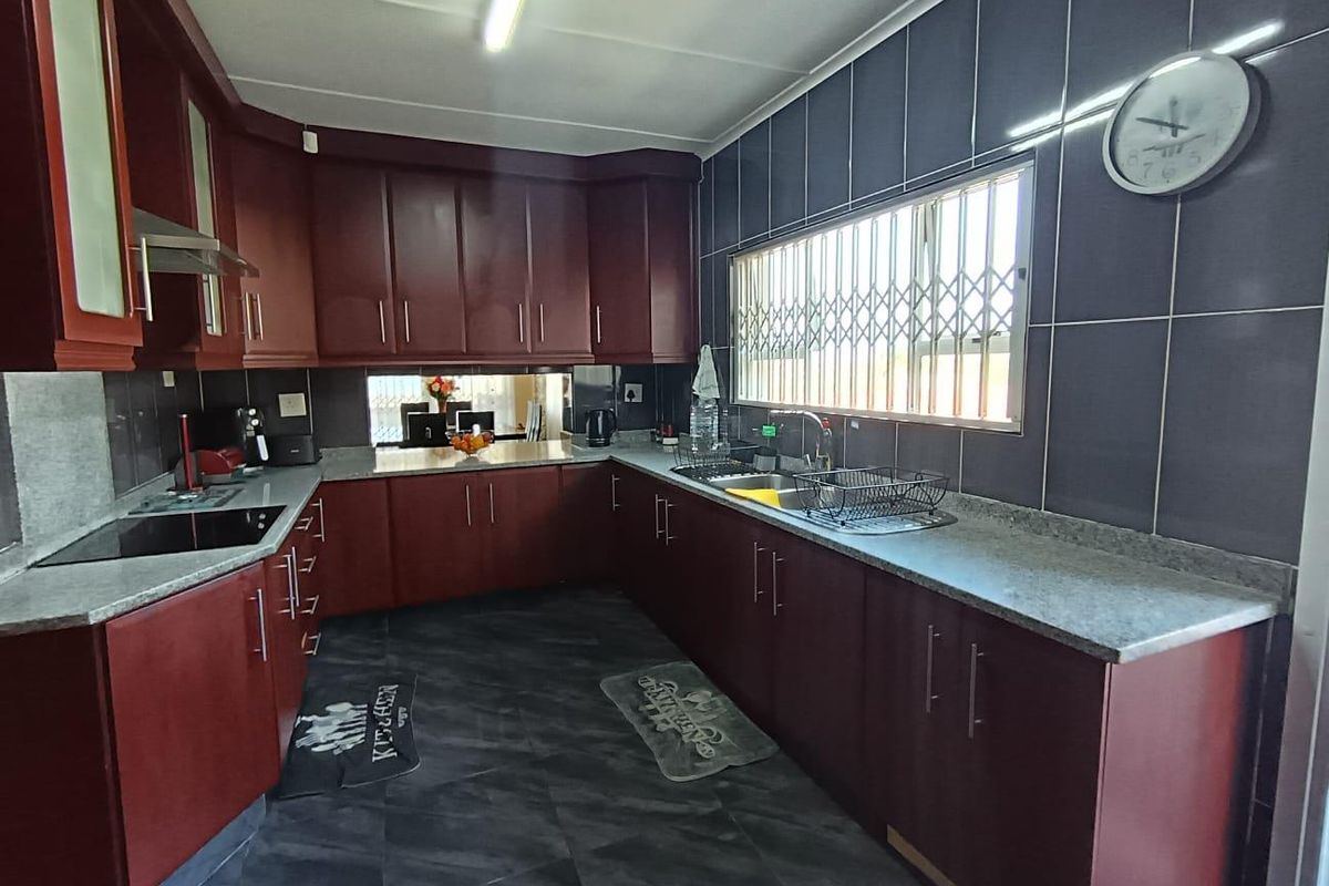 A functional kitchen featuring dark wood cabinetry, granite-look laminate countertops, a stainless steel sink, and a built-in electric hob with an extractor fan.