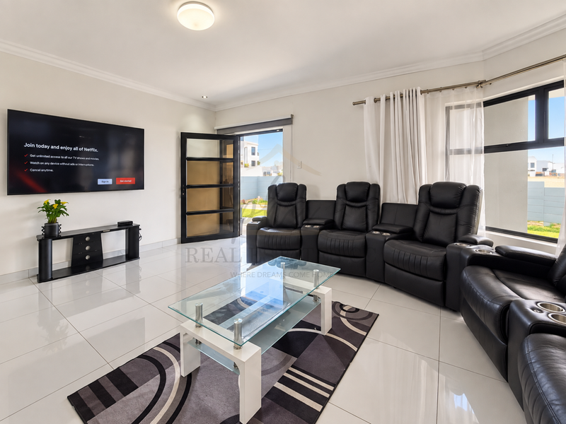 A bright, modern living room featuring polished porcelain floor tiles, large aluminium windows, and a glass panel door leading to the exterior.