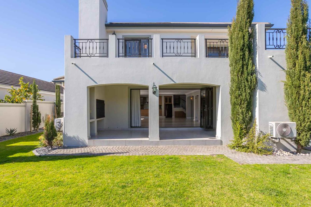 Rear view of the property featuring a covered patio, upper balcony with wrought iron railings, bi-fold doors, and a well-maintained garden.