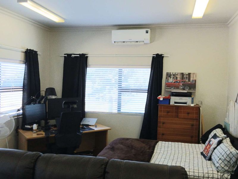 A functional bedroom featuring a split-system air conditioner, venetian blinds, and overhead fluorescent lighting.
