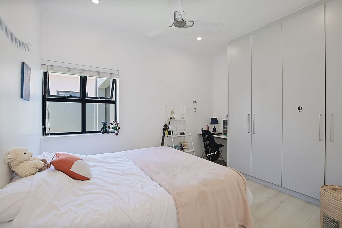 A bright bedroom featuring built-in floor-to-ceiling wardrobes, a ceiling fan, and modern window frames with roller blinds.