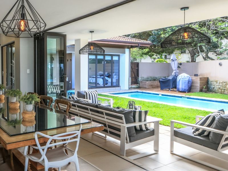 A spacious covered patio featuring tiled flooring and seamless indoor-outdoor flow, overlooking a private swimming pool and landscaped garden area.