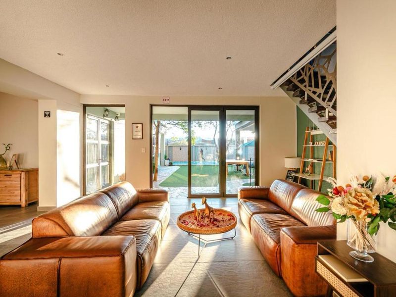 Spacious living room featuring tiled flooring, recessed lighting, and a decorative staircase, with large sliding glass doors providing direct access to the outdoor pool area.