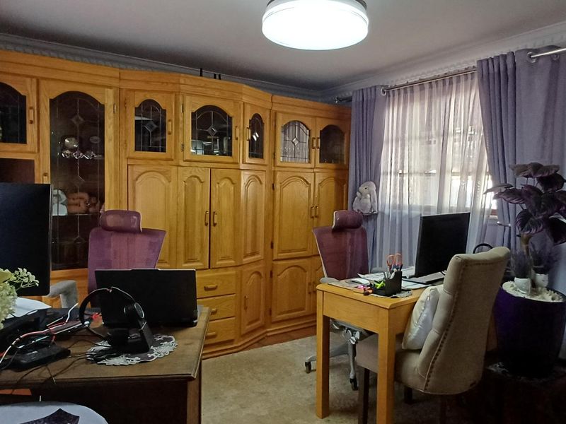 A home office featuring extensive built-in wooden cabinetry, crown molding, and natural light through window treatments.