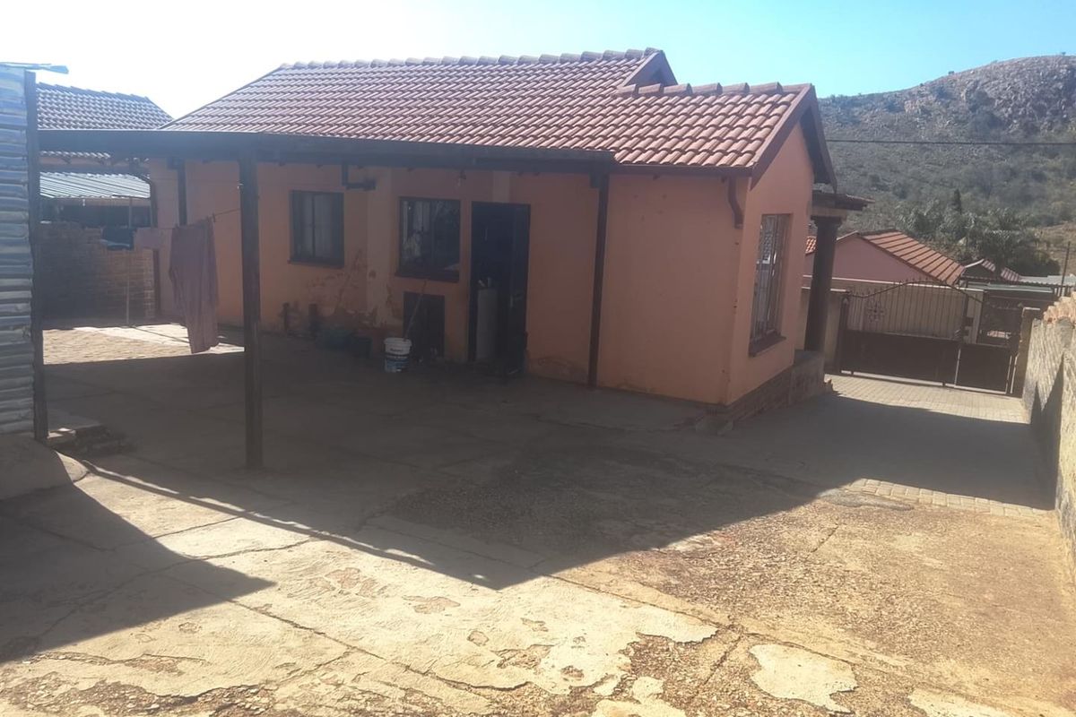 Rear view of the property featuring a covered patio area, tiled roof, and a concrete driveway with visible wear.
