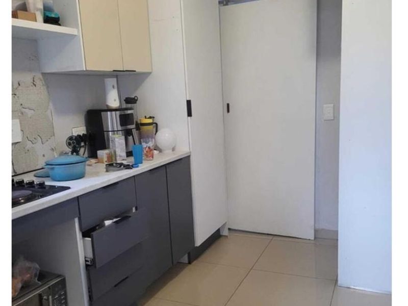 Compact kitchen featuring two-tone cabinetry, tiled flooring, and a sliding door, currently requiring maintenance and cosmetic repairs to the wall and cabinetry.