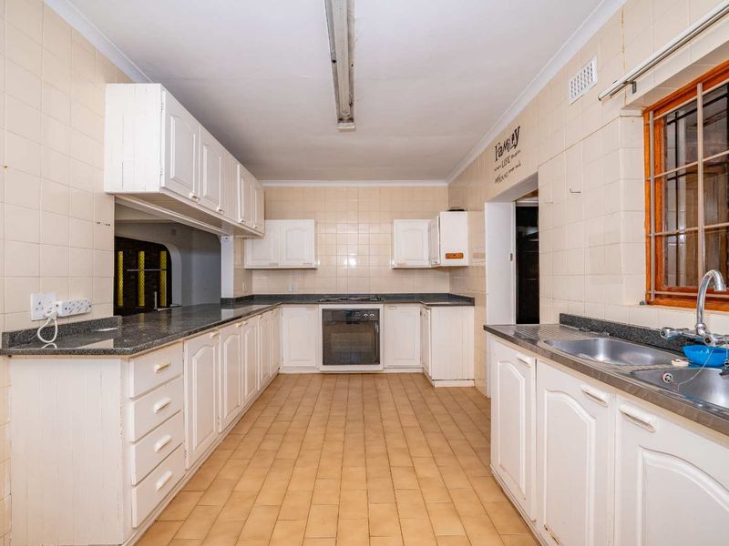 A spacious, dated kitchen featuring white built-in cabinetry, granite countertops, a double basin sink, and a built-in oven with hob.