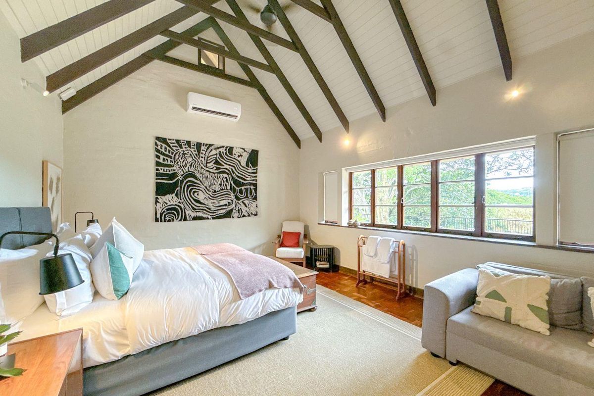 Spacious bedroom featuring high vaulted ceilings with exposed timber beams, terracotta flooring, and a wall-mounted air conditioning unit.