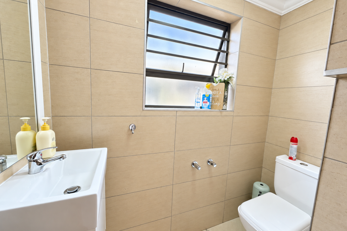 A clean, modern bathroom featuring neutral wall tiles, a wall-mounted basin with chrome fixtures, and a louvered window for natural ventilation.