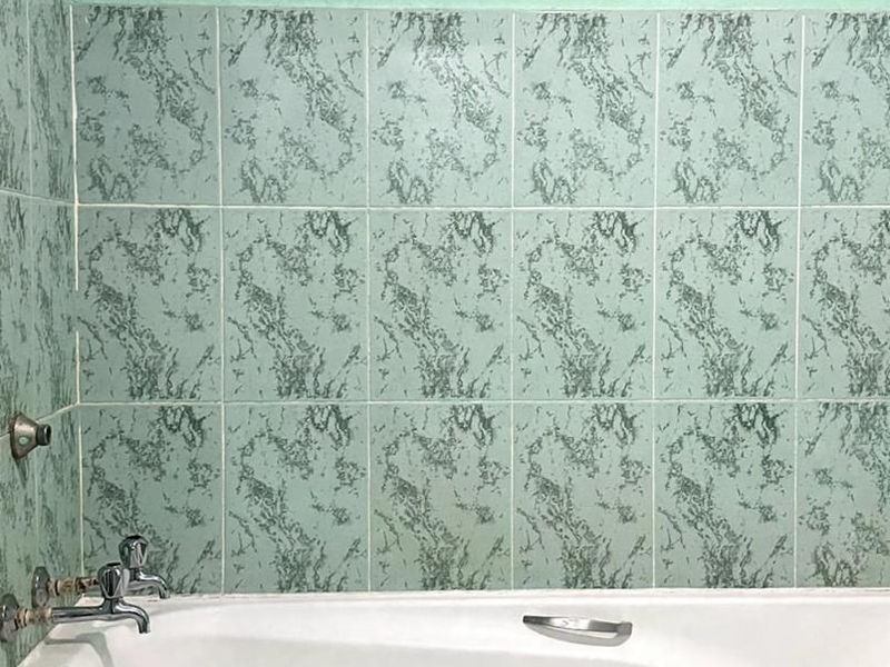 A bathroom featuring a standard white bathtub with chrome fixtures and patterned green wall tiles.