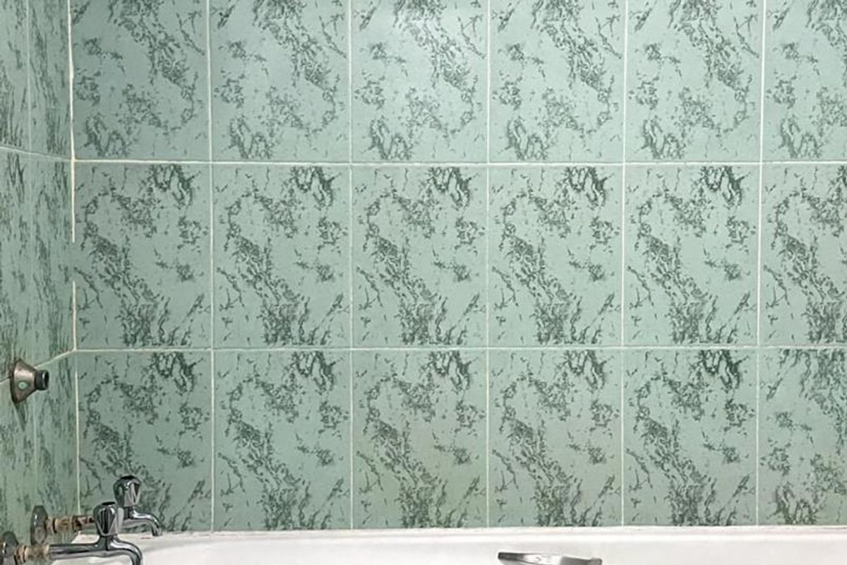 A bathroom featuring a standard white bathtub with chrome fixtures and patterned green wall tiles.