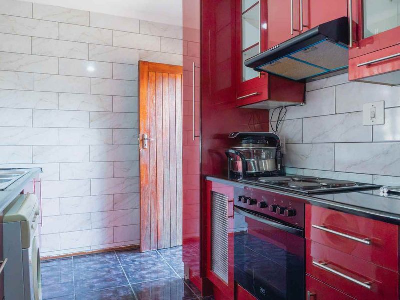 A functional kitchen featuring high-gloss red cabinetry, a built-in oven with hob, extractor fan, and modern tiled wall finishes.