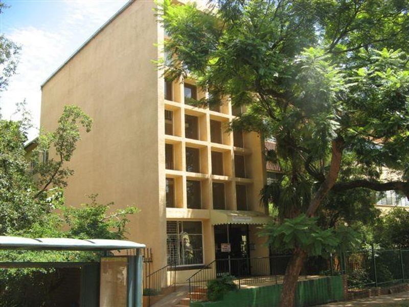 Exterior view of a multi-story apartment building featuring a distinctive grid-patterned facade, entrance awning, and mature surrounding trees.