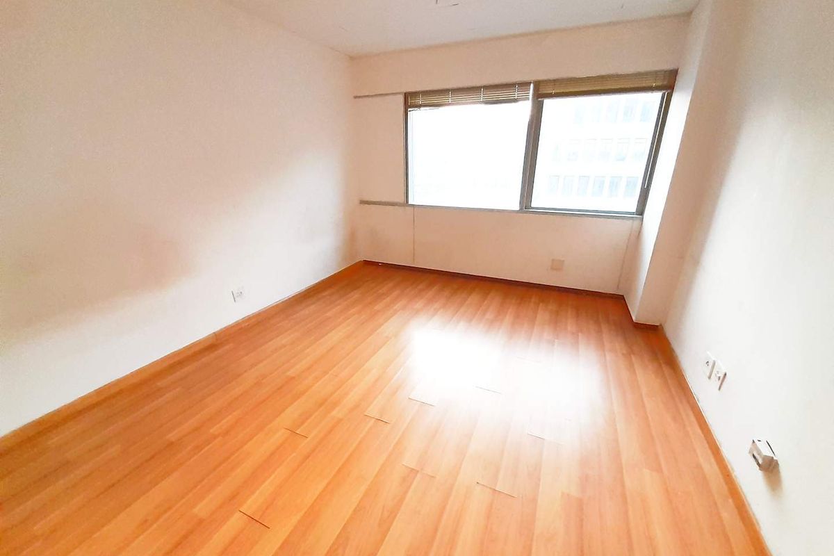 An empty bedroom featuring laminate flooring and a large window with fitted blinds, offering a blank canvas for personalization.