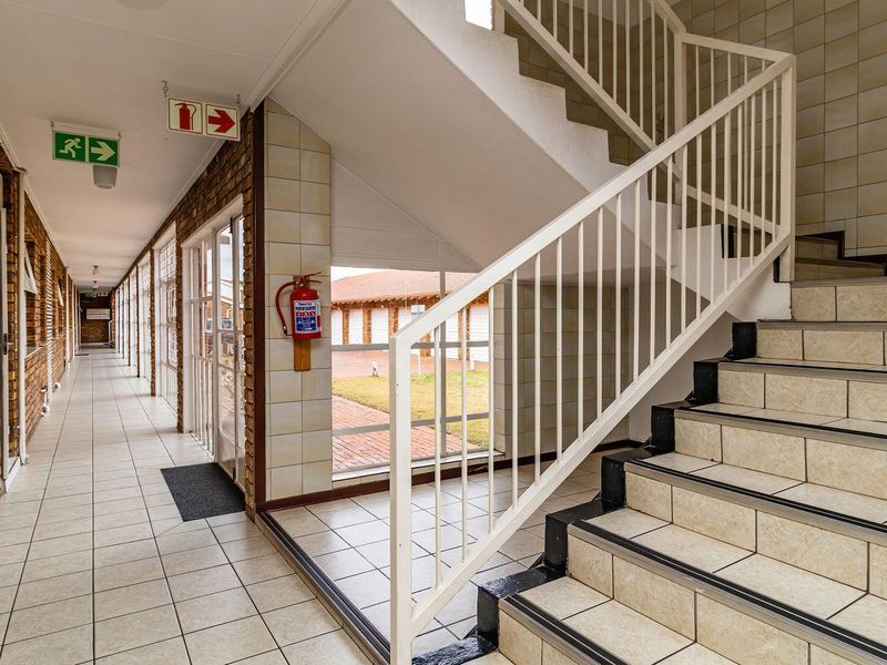 A clean, well-maintained communal hallway featuring tiled flooring, exposed brick walls, and a staircase with a metal balustrade.