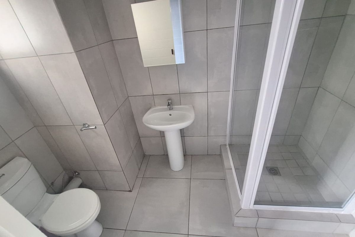 A clean, modern bathroom featuring a pedestal basin, a glass-enclosed shower, and neutral floor-to-ceiling tiling.