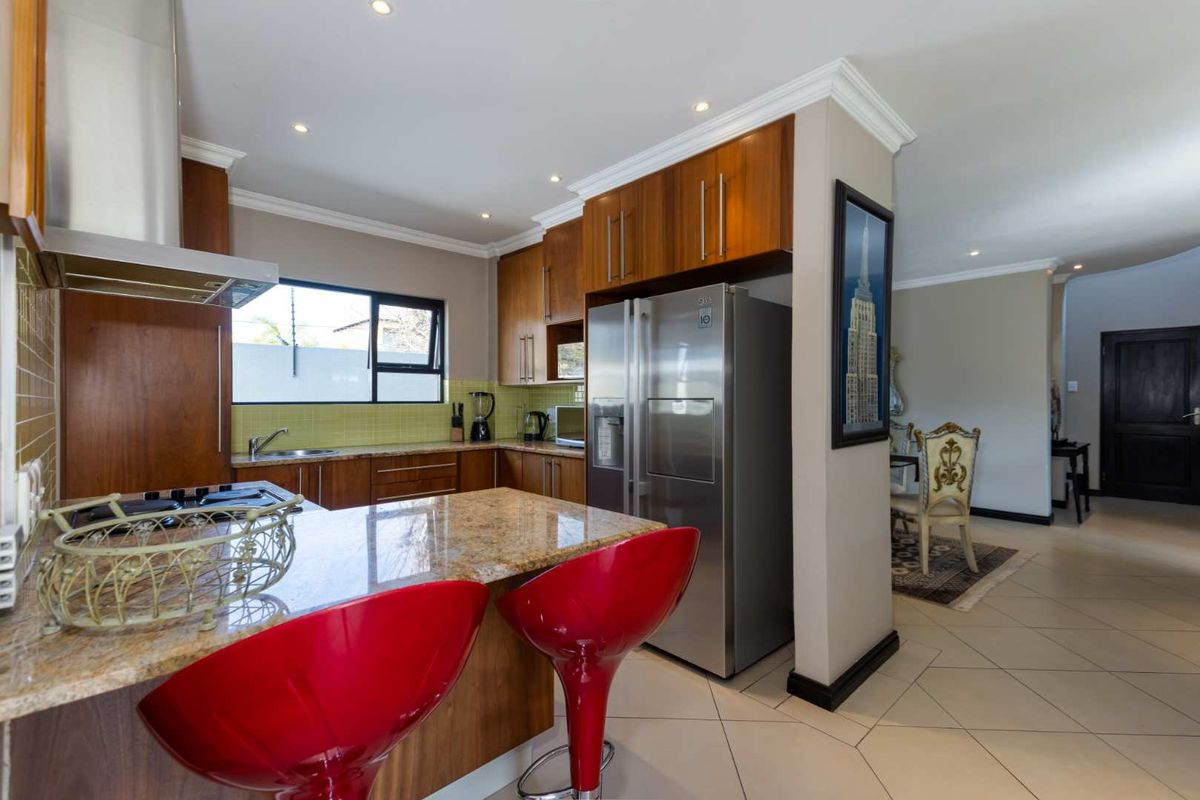 A functional kitchen featuring wood cabinetry, granite countertops, a stainless steel extractor fan, and tiled flooring, seamlessly flowing into the adjacent dining area.