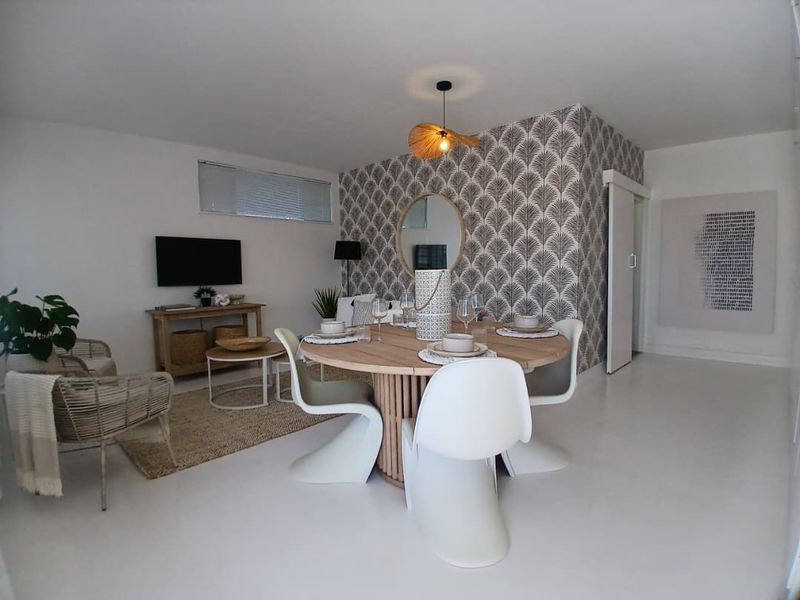 An open-plan living and dining area featuring modern white flooring, a decorative feature wall with patterned wallpaper, and a contemporary pendant light fixture.