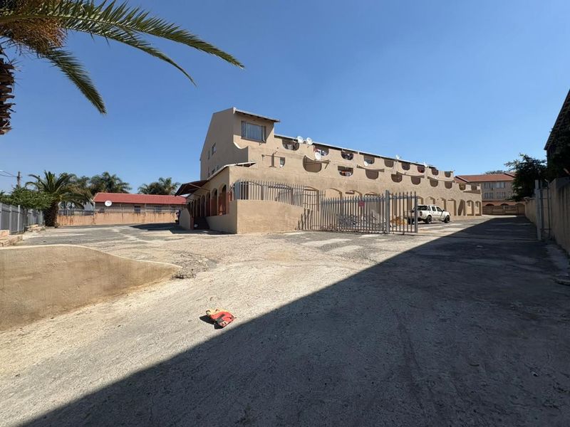 Rear view of the apartment complex showing the paved parking area, security fencing, and building facade with multiple satellite dish installations.