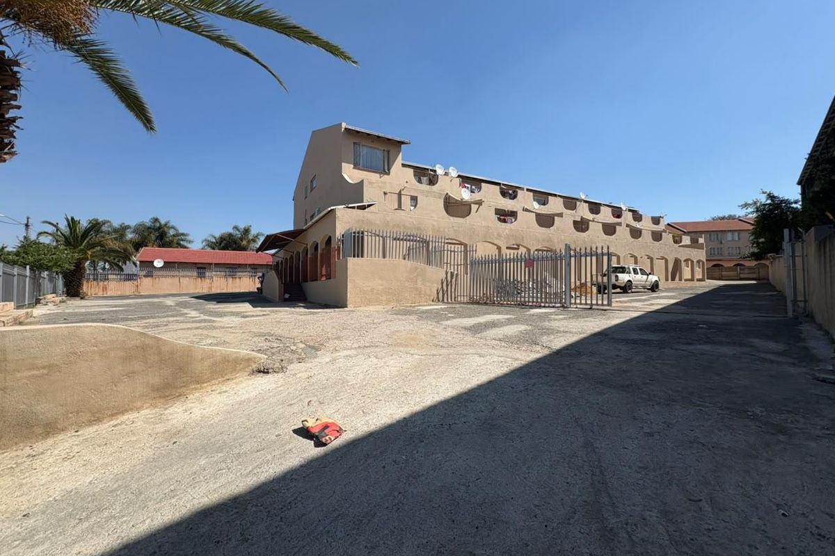 Rear view of the apartment complex showing the paved parking area, security fencing, and building facade with multiple satellite dish installations.