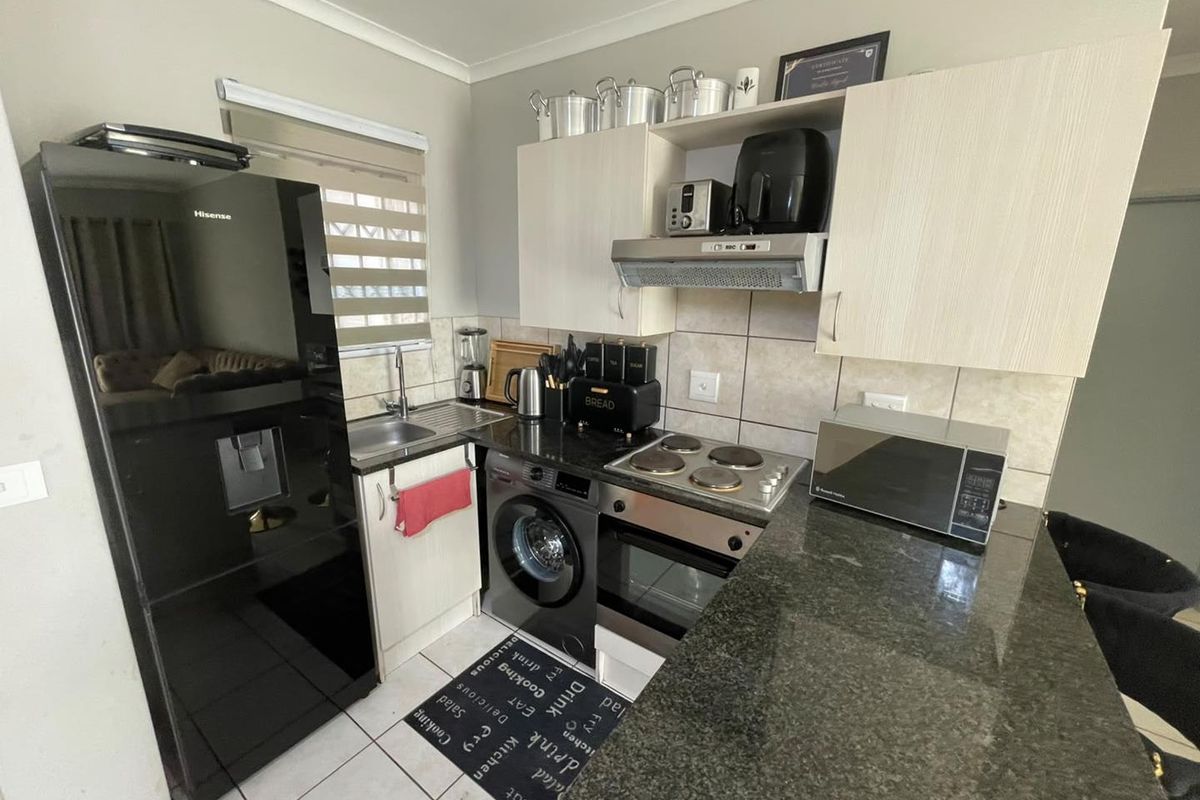 Compact kitchen featuring granite countertops, built-in oven with electric hob, extractor fan, and tiled backsplash with ample cabinetry.