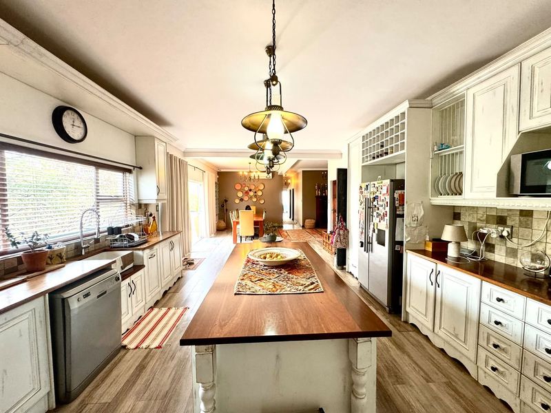 Spacious open-plan kitchen featuring a large central island with wooden countertop, ample cabinetry, and integrated appliances, flowing into the dining area.