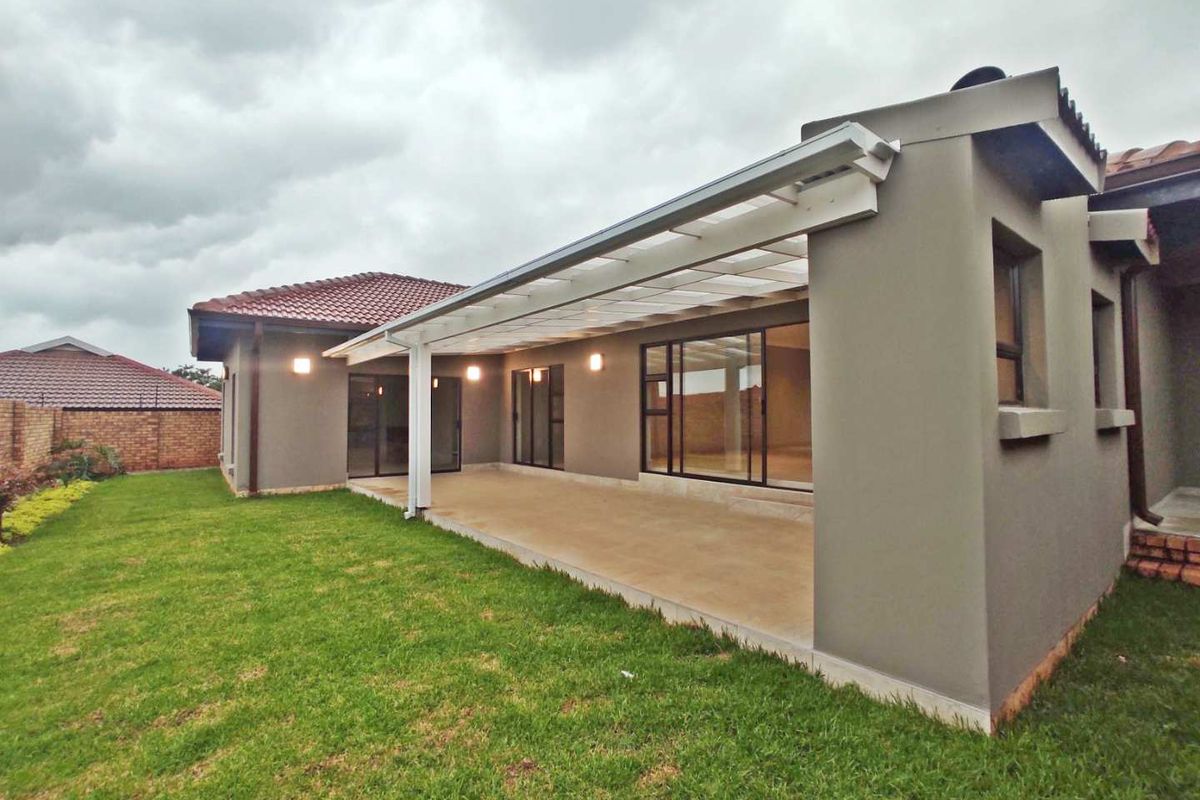 A well-maintained rear exterior view featuring a spacious covered patio with concrete flooring, sliding glass doors, and a neat lawn area.