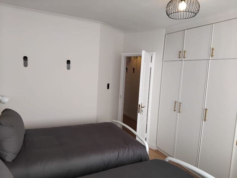 A well-maintained bedroom featuring built-in cupboards with modern hardware, hardwood flooring, and neutral wall finishes.