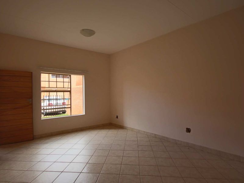 An empty bedroom featuring tiled flooring, a window with security bars, and a wooden door, presenting a blank canvas for personalization.