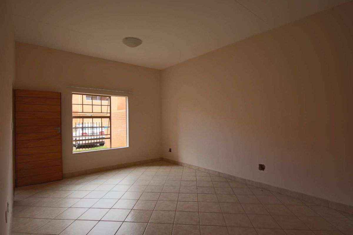 An empty bedroom featuring tiled flooring, a window with security bars, and a wooden door, presenting a blank canvas for personalization.