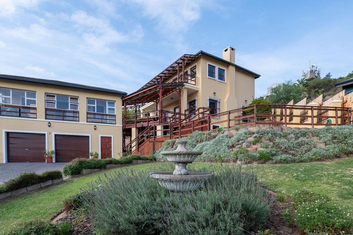A multi-level residential property featuring a double garage, expansive wooden decking, and a landscaped garden with a central stone fountain.