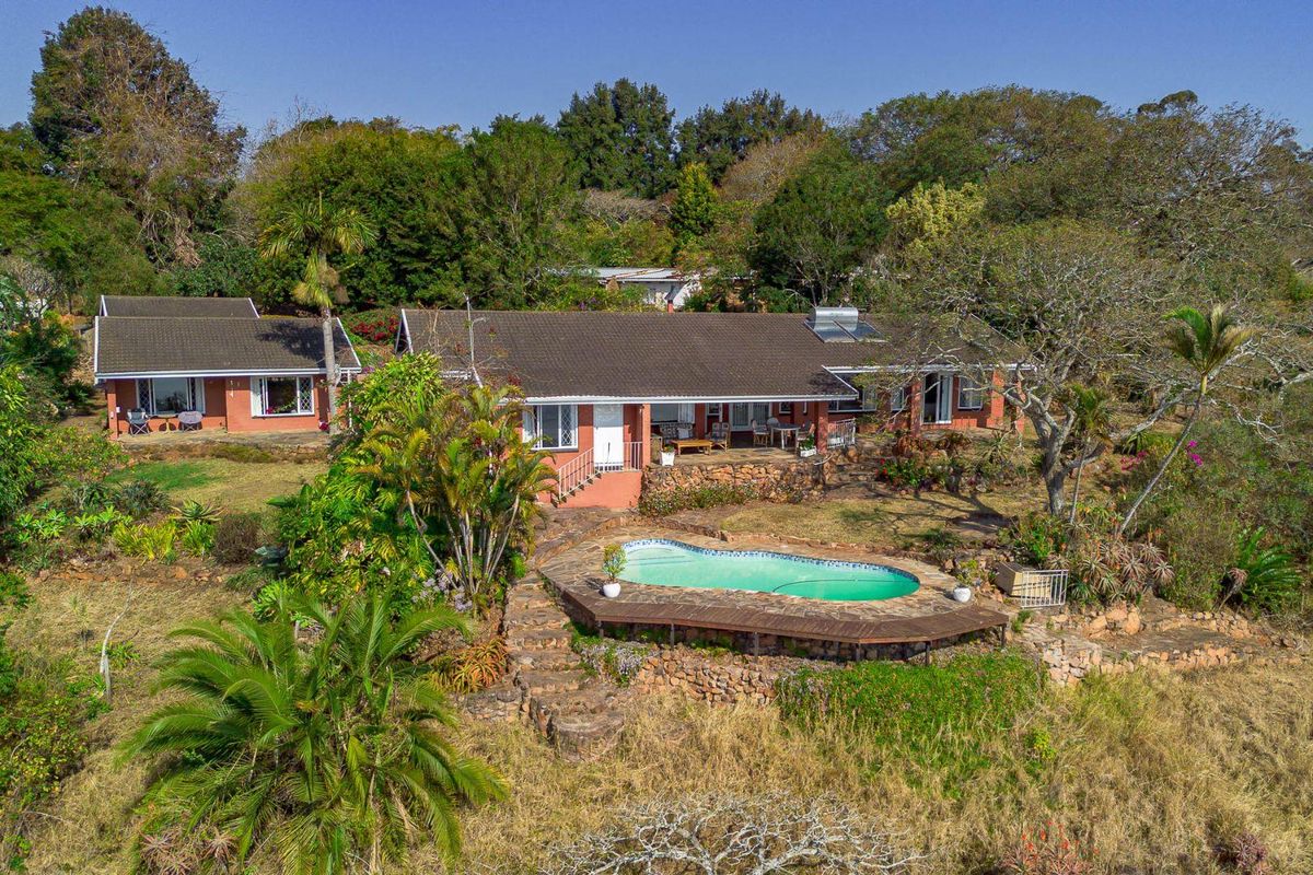 Aerial view of a residential property featuring a swimming pool, wooden decking, stone retaining walls, and a tiled roof set within a large garden.